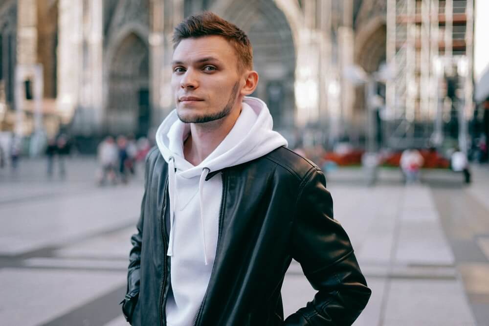 Pria mengenakan hoodie berwarna putih, yang dilapisi dengan jaket kulit berwarna hitam.